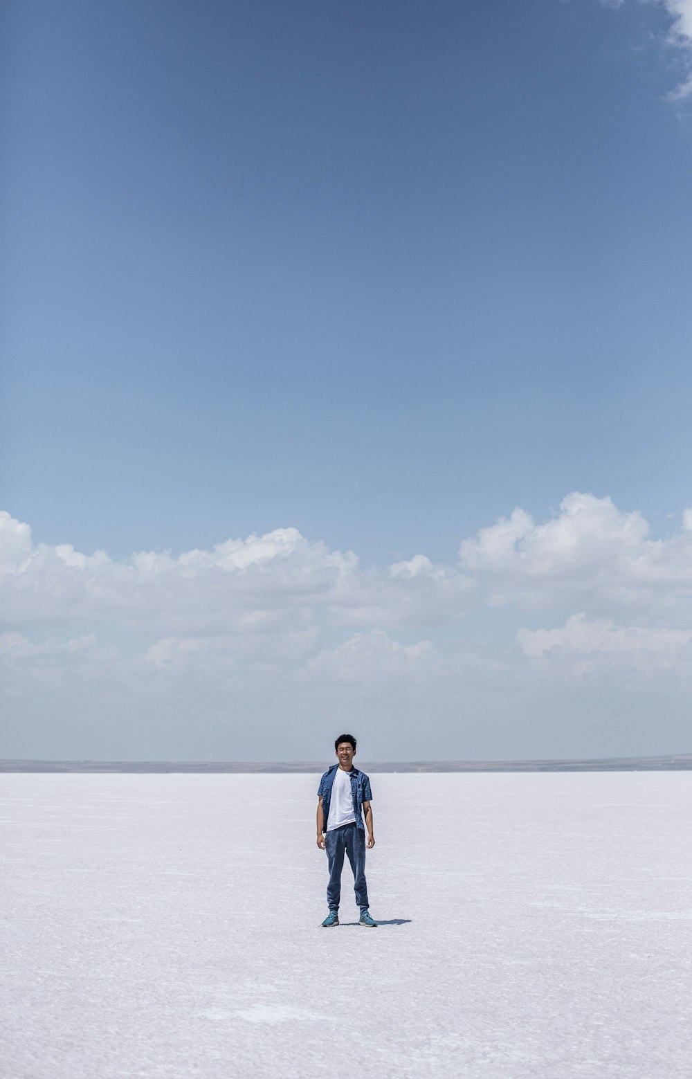 man in white shirt and blue denim jeans standing on beach during daytime