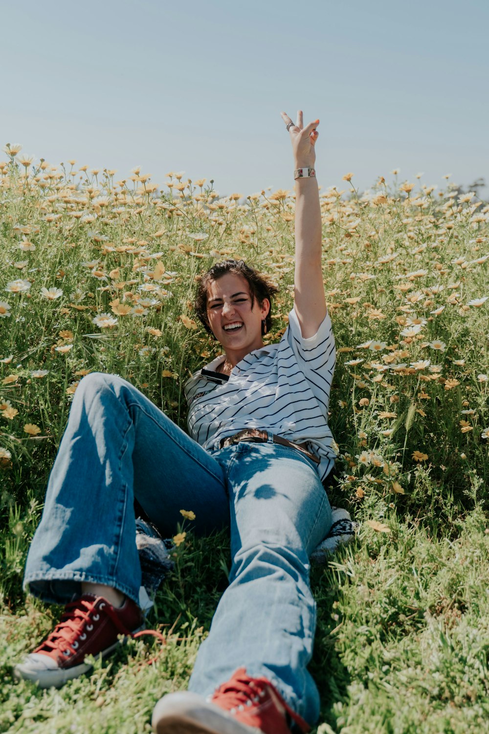 woman in white t-shirt and blue denim jeans lying on green grass field during daytime
