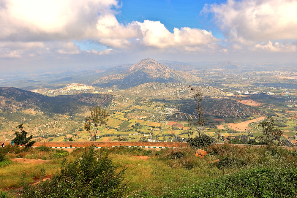 green grass field near mountain under white clouds and blue sky during daytime