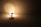 A decorative lamp with a floral design emits a soft, warm light. The lamp is positioned on a smooth surface, casting light and subtle shadows in a dimly lit room. The metal base and stem add a modern touch to the lamp's intricate design.