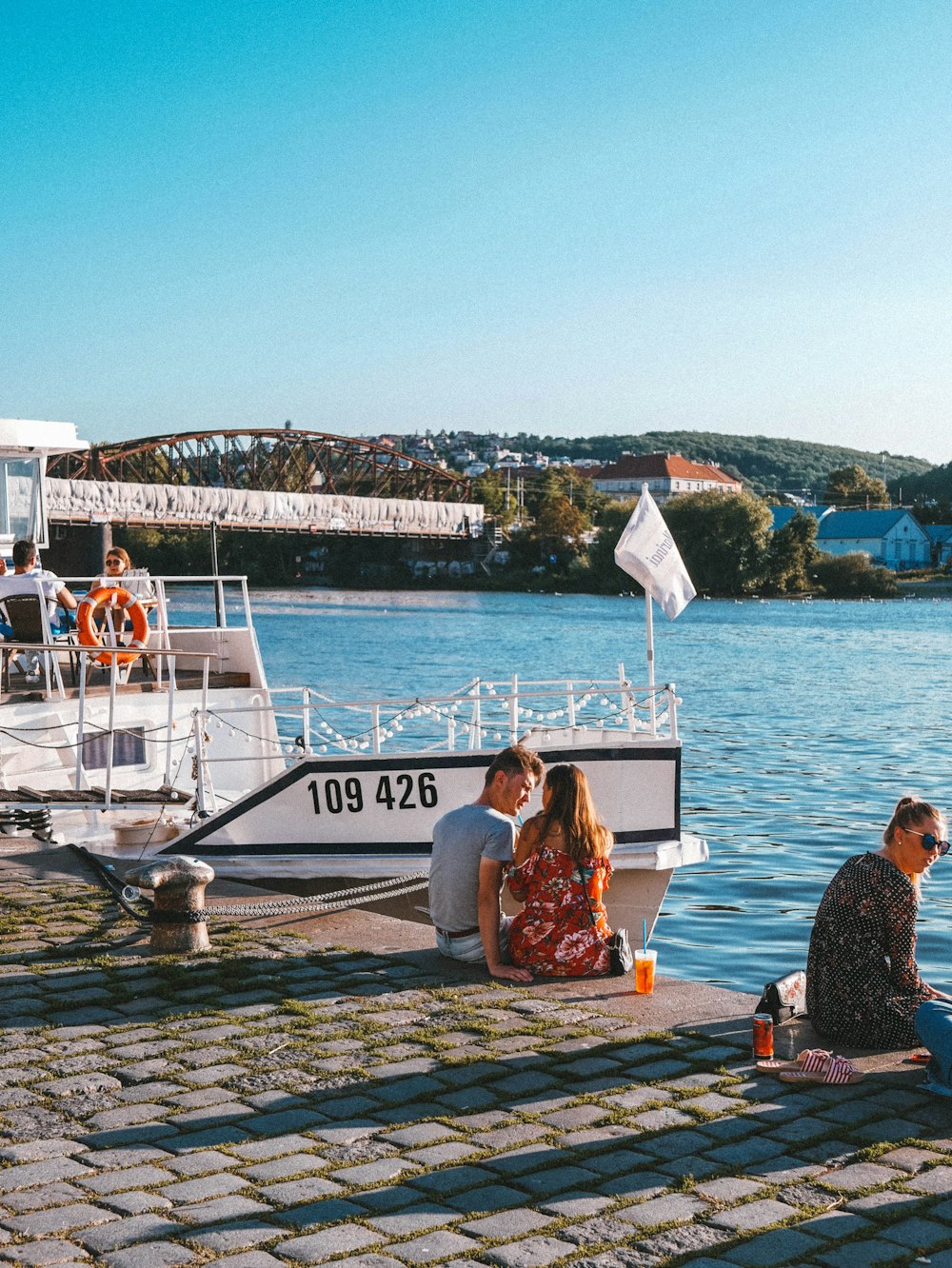 man and woman sitting on brown wooden bench near body of water during daytime