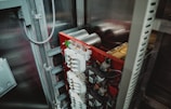 An electrical panel with several circuit breakers and transformers installed inside an industrial cabinet. The panel has a red backing and is surrounded by metal framing. Various wires and components are visible, indicating a complex setup.