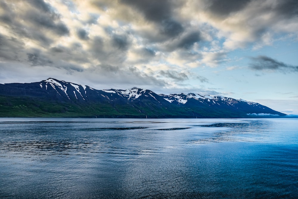 body of water near mountain under cloudy sky during daytime