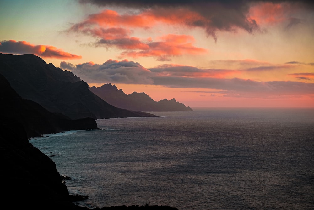 body of water near mountain during sunset