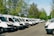 A smiling fleet manager standing beside a row of eco-friendly trucks under a clear blue sky.
