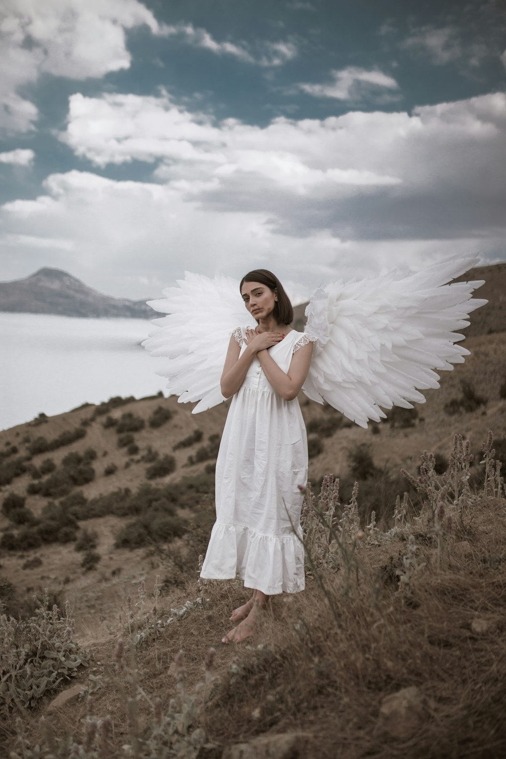 woman in white dress standing on brown grass field near body of water during daytime