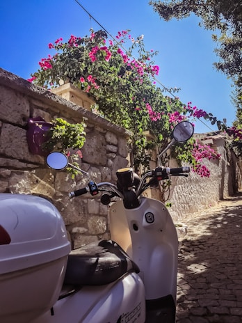 A scooter resting beside a traditional whitewashed building adorned with bougainvillea.