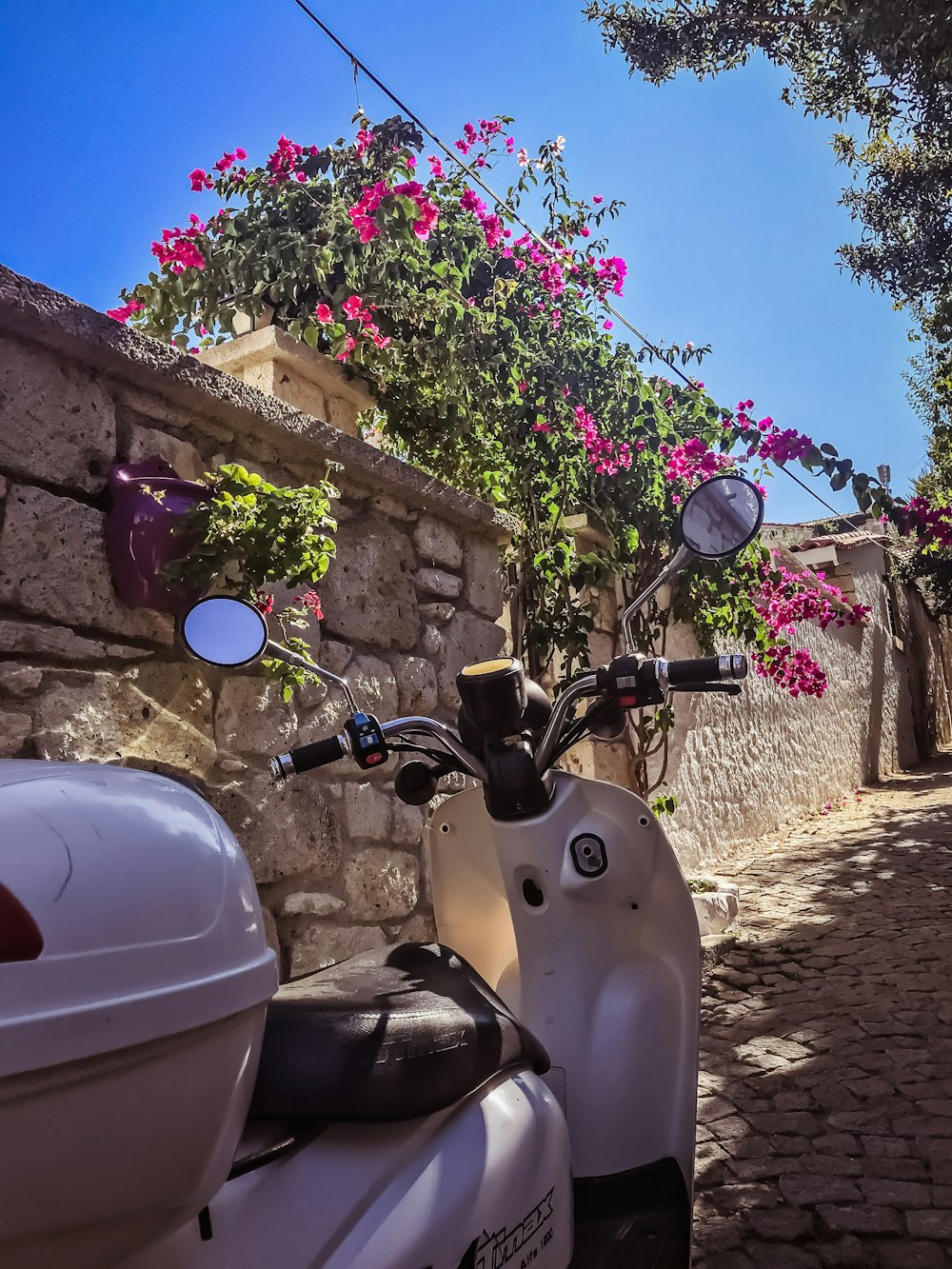 white and black motor scooter parked beside brown concrete wall during daytime