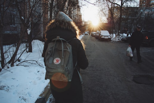 woman in black jacket and brown backpack standing on road during daytime