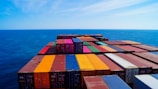 A vast array of colorful shipping containers stacked on the deck of a cargo ship, set against the expansive blue ocean and sky.