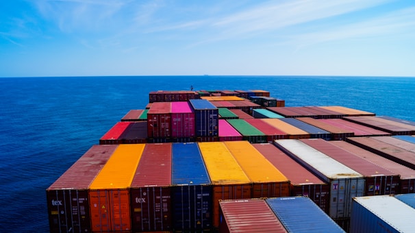A vast array of colorful shipping containers stacked on the deck of a cargo ship, set against the expansive blue ocean and sky.