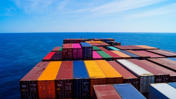 A vast array of colorful shipping containers stacked on the deck of a cargo ship, set against the expansive blue ocean and sky.