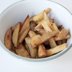 Sliced potato wedges with a roasted or baked appearance in a white bowl with a green rim.