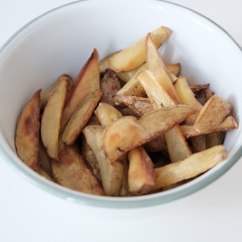Sliced potato wedges with a roasted or baked appearance in a white bowl with a green rim.