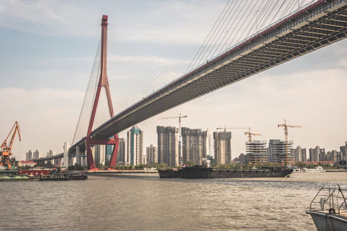 Modern bridge construction over a river with cranes in the background.
