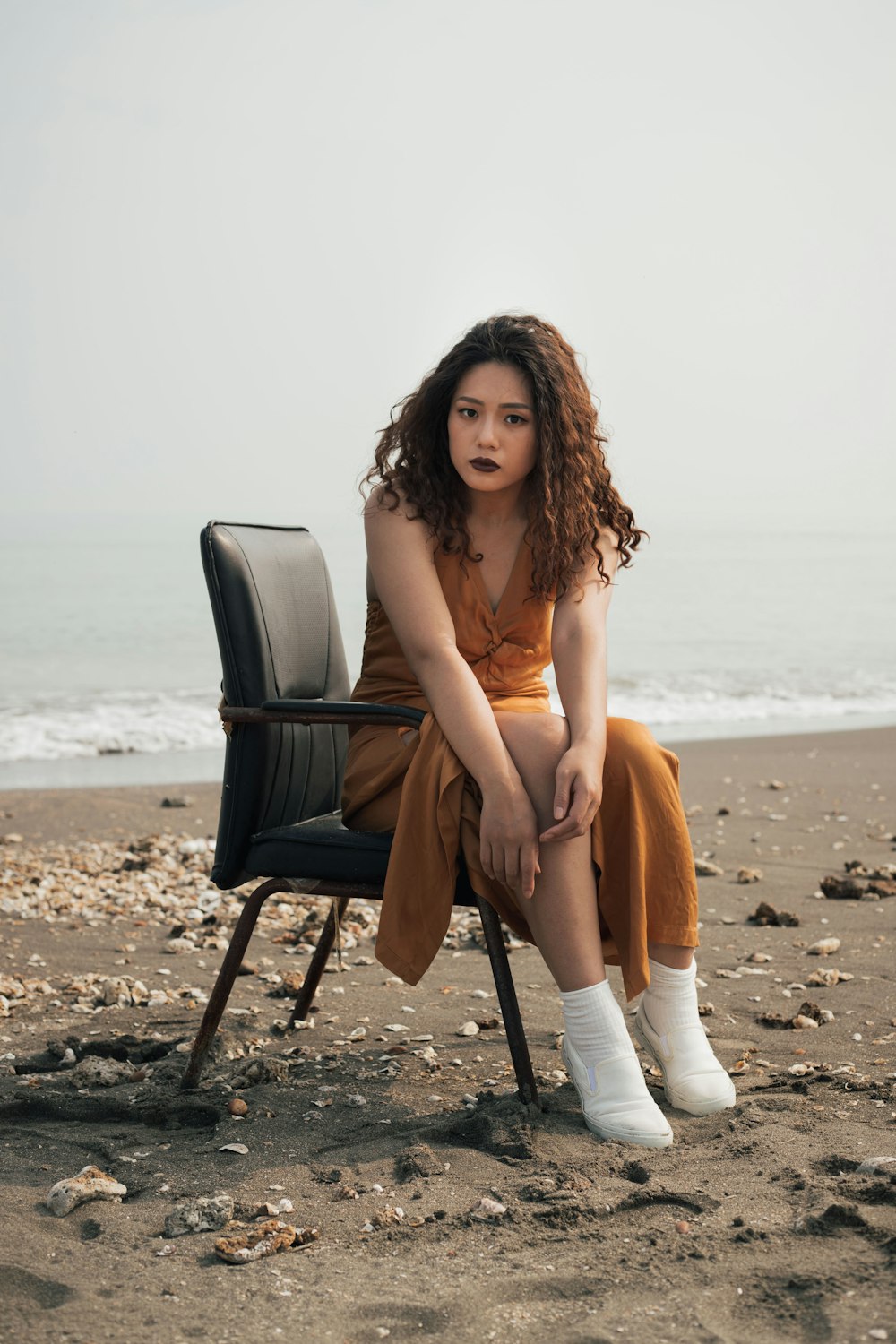 woman in brown sleeveless dress sitting on black chair on beach during daytime