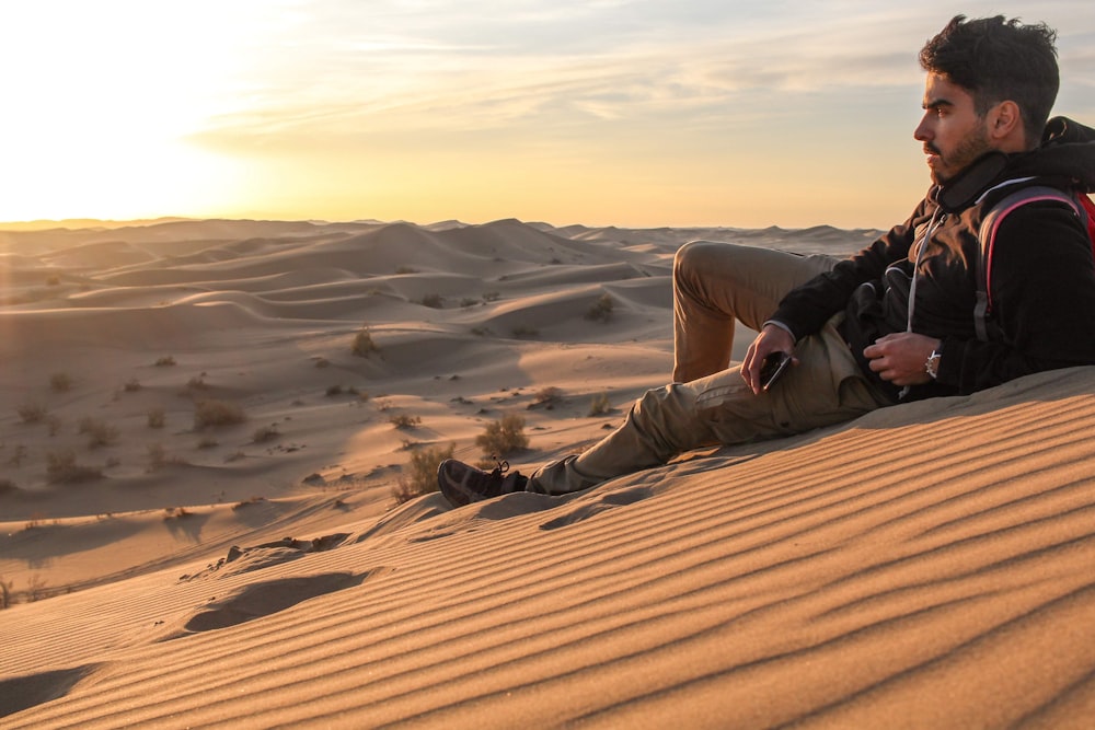 person in black jacket and brown pants sitting on sand during daytime