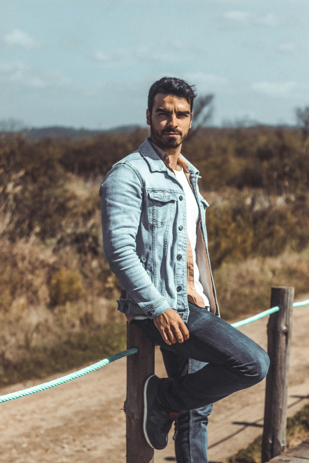 man in blue denim jacket sitting on blue metal fence during daytime