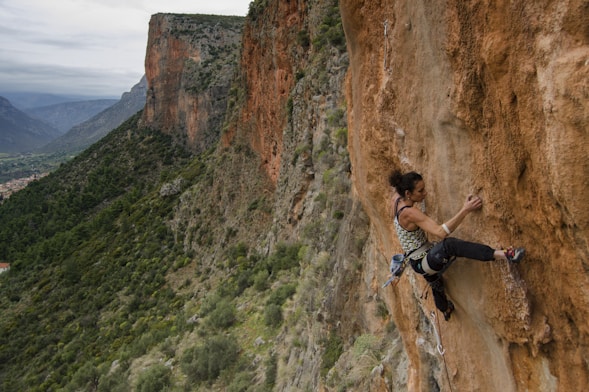 woman in black tank top climbing on brown rocky mountain during daytime