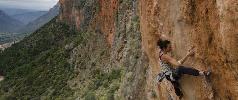 woman in black tank top climbing on brown rocky mountain during daytime
