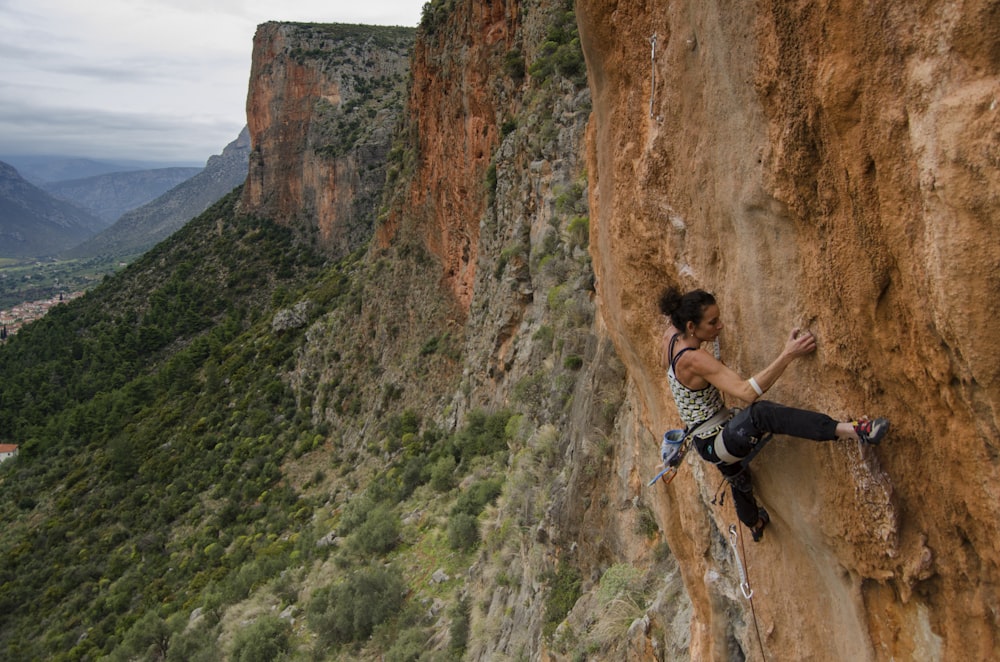 Mujer en camiseta sin mangas negra escalando en la montaña rocosa marrón durante el día