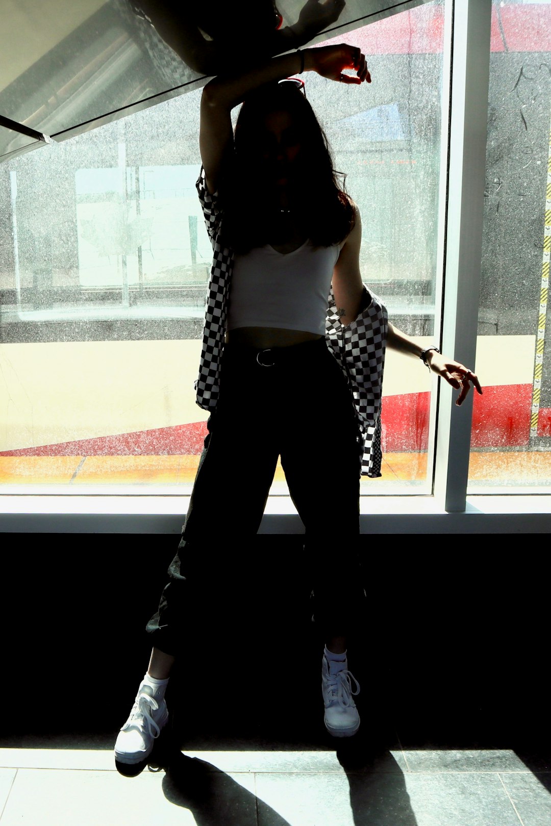 woman in white tank top and black pants standing beside glass window