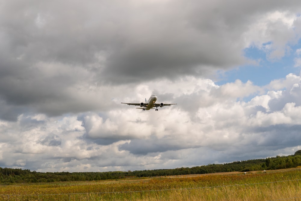 airplane flying over green grass field under white clouds during daytime