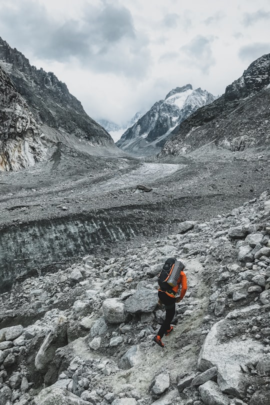 person in orange jacket and black pants walking on rocky road during daytime in Mer de Glace France