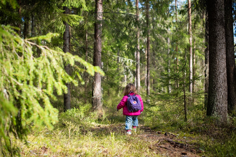 girl in red jacket walking on forest during daytime