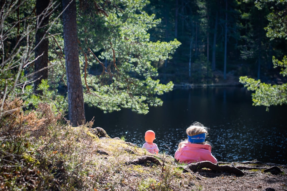 woman in red jacket sitting on rock near lake during daytime