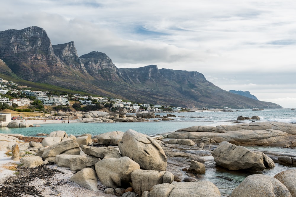 brown rocks on seashore near mountain under white clouds during daytime