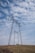 Several large electricity pylons stand on a grassy hill beneath a partly cloudy sky. A small green van is parked near the base of the closer pylon.