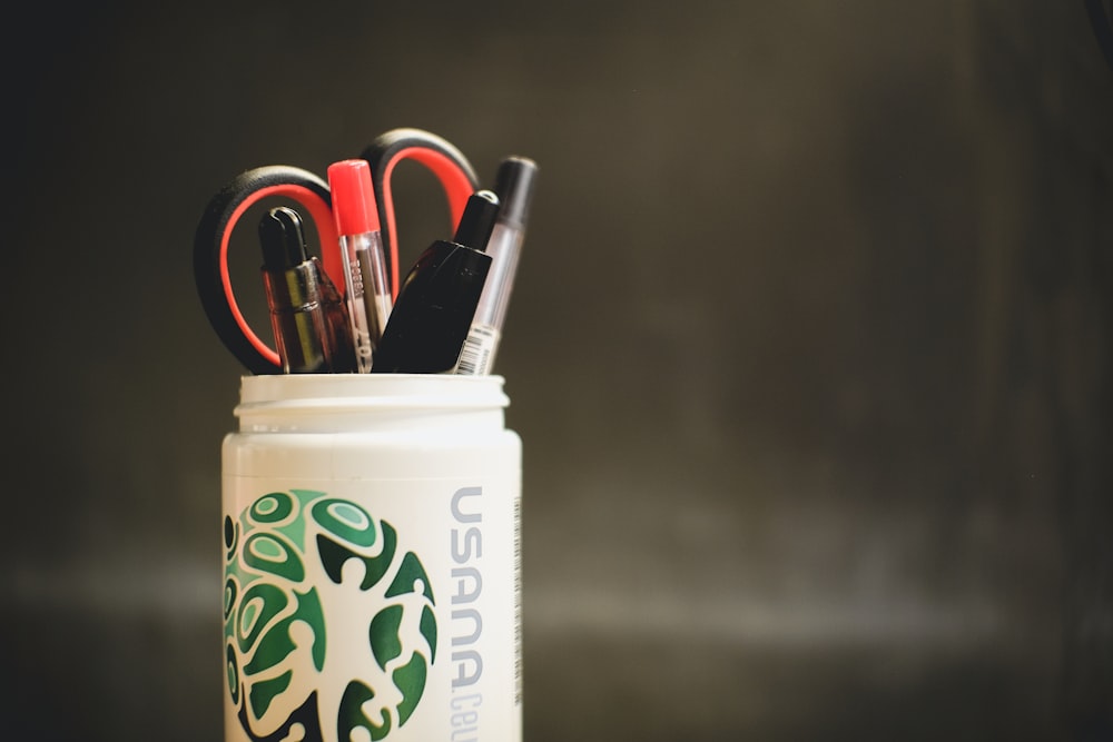 white and blue plastic cup with pens and pencils