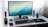 A modern computer setup on a white desk, featuring a widescreen monitor displaying a blue gradient wallpaper. Two gaming controllers are placed on stands underneath the monitor. A mechanical keyboard and a wireless mouse sit in front of the monitor on a mouse pad. A smartphone is lying next to a small potted plant on the left, and there is a smart speaker nearby. The desk is flanked by a sleek desk lamp and two speakers, with sheer white curtains in the background.