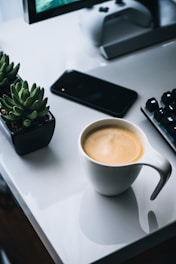 white ceramic mug beside black iphone 4