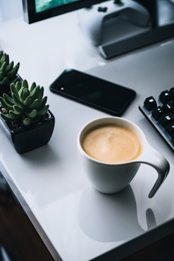 white ceramic mug beside black iphone 4