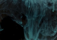 Teal liquid tendrils twisting gracefully in slow motion, set against an inky black backdrop.