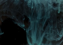Swirling, wavy, translucent teal-colored shapes against a dark background creating a mystical and ethereal visual effect.