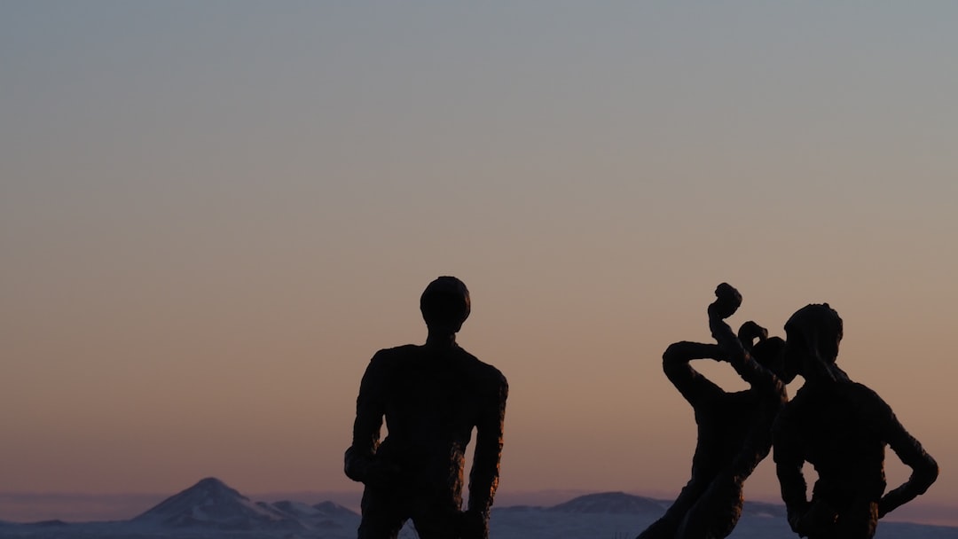 silhouette of man and woman standing on rock formation during sunset