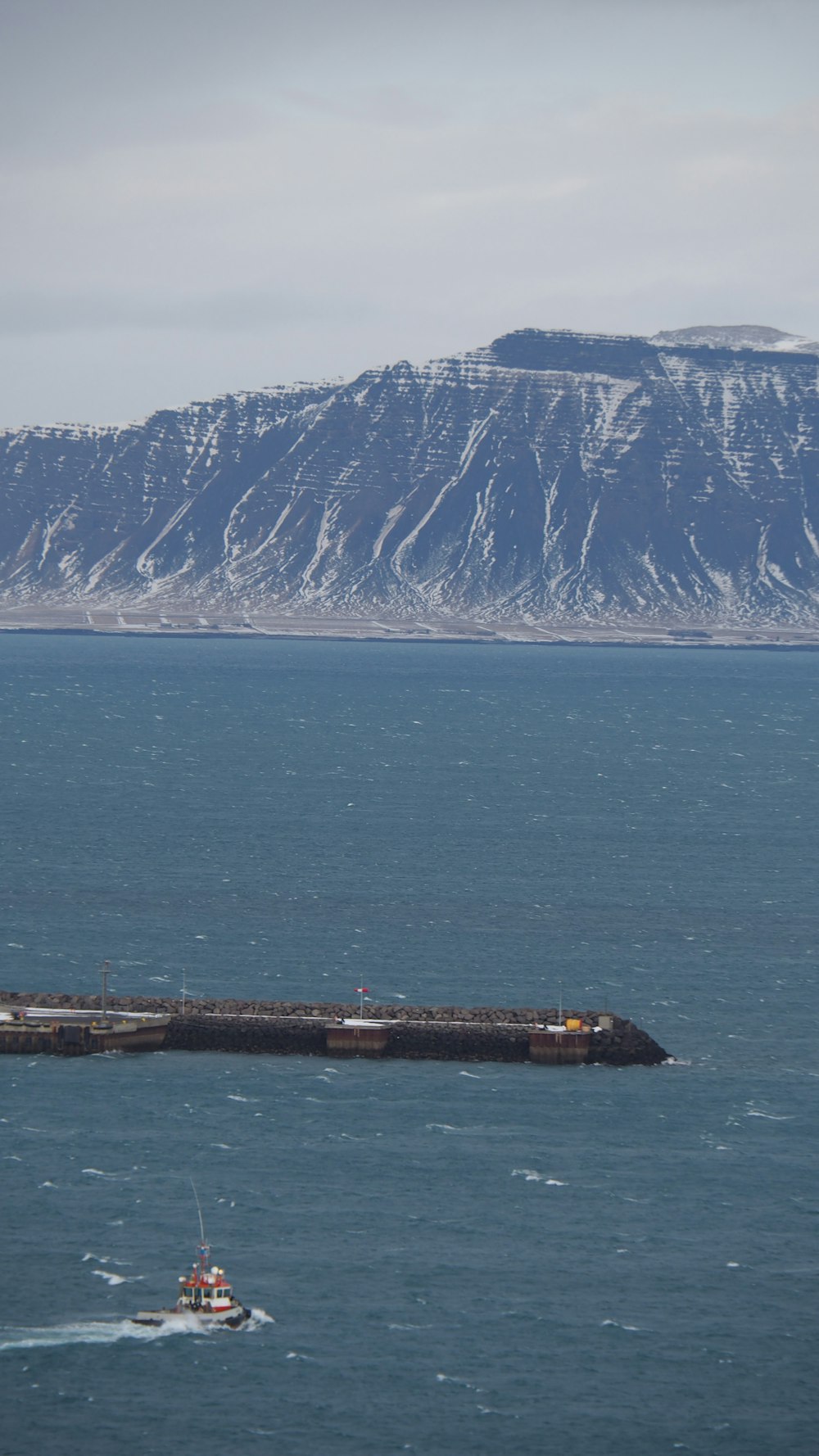 Muelle de madera marrón en el cuerpo de agua cerca de la montaña cubierta de nieve durante el día