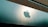 A large, reflective building facade featuring a prominent and shiny apple logo. The facade is composed of smooth, metallic panels with a modern architectural style. The upper portion of the building consists of a more textured, darker material that contrasts with the sleek panels below.