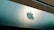 A large, reflective building facade featuring a prominent and shiny apple logo. The facade is composed of smooth, metallic panels with a modern architectural style. The upper portion of the building consists of a more textured, darker material that contrasts with the sleek panels below.