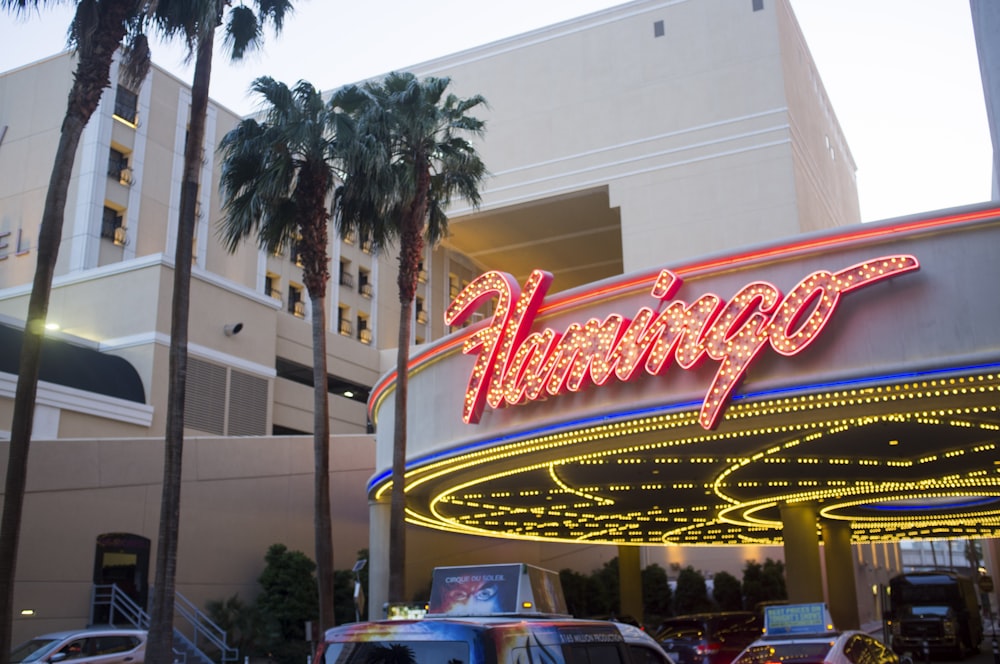 a building with a neon sign and palm trees in front of it