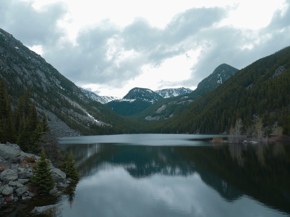 lago cercado por montanhas verdes sob o céu branco durante o dia