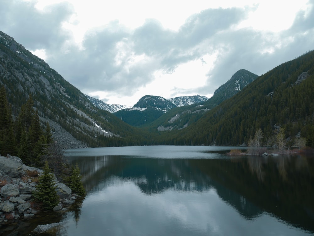 lake surrounded by green mountains under white sky during daytime