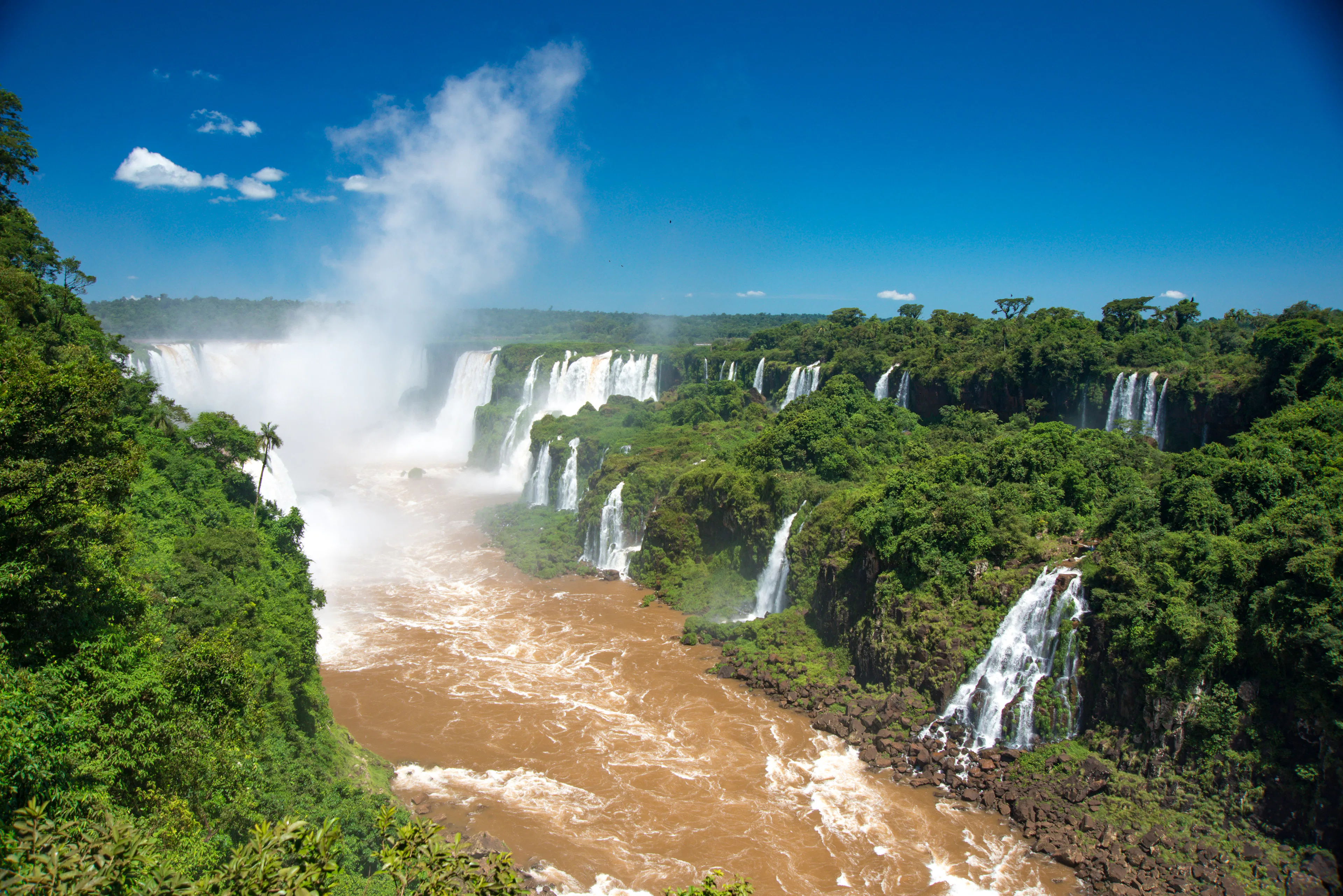 Garganta del Diablo en las Cataratas del Iguazú, con nube de rocío, selva verde y cielo azul