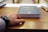 person holding black covered book on brown wooden table