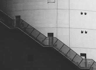 A large industrial structure with a smooth, curved concrete surface, featuring a metal staircase with a mesh pattern. The surface is dotted with small fixtures and squared openings.