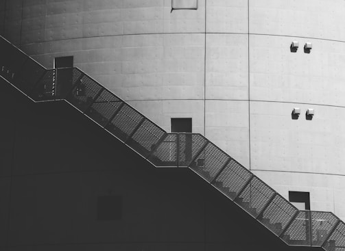 A large industrial structure with a smooth, curved concrete surface, featuring a metal staircase with a mesh pattern. The surface is dotted with small fixtures and squared openings.