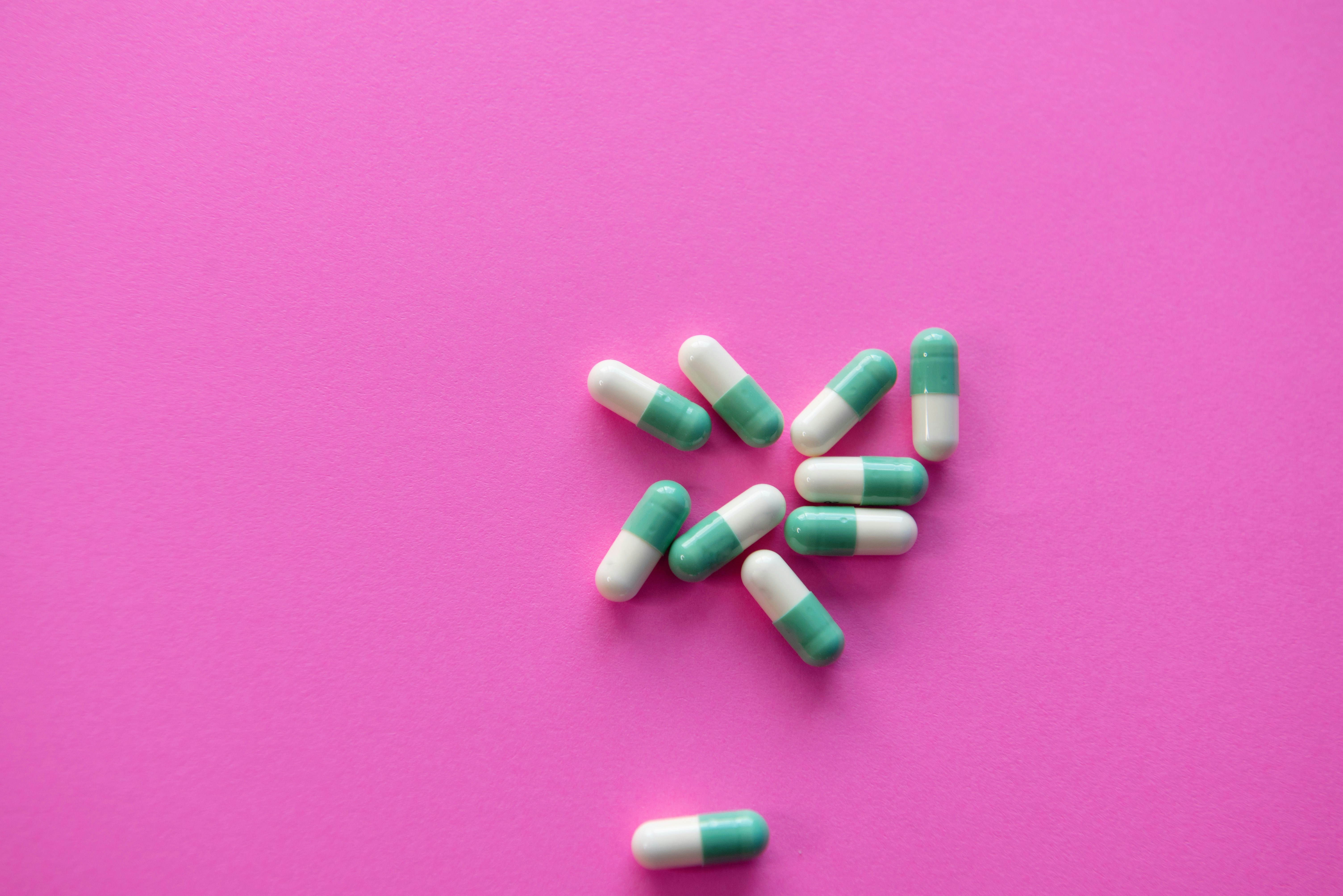 white and blue medication pill on pink textile